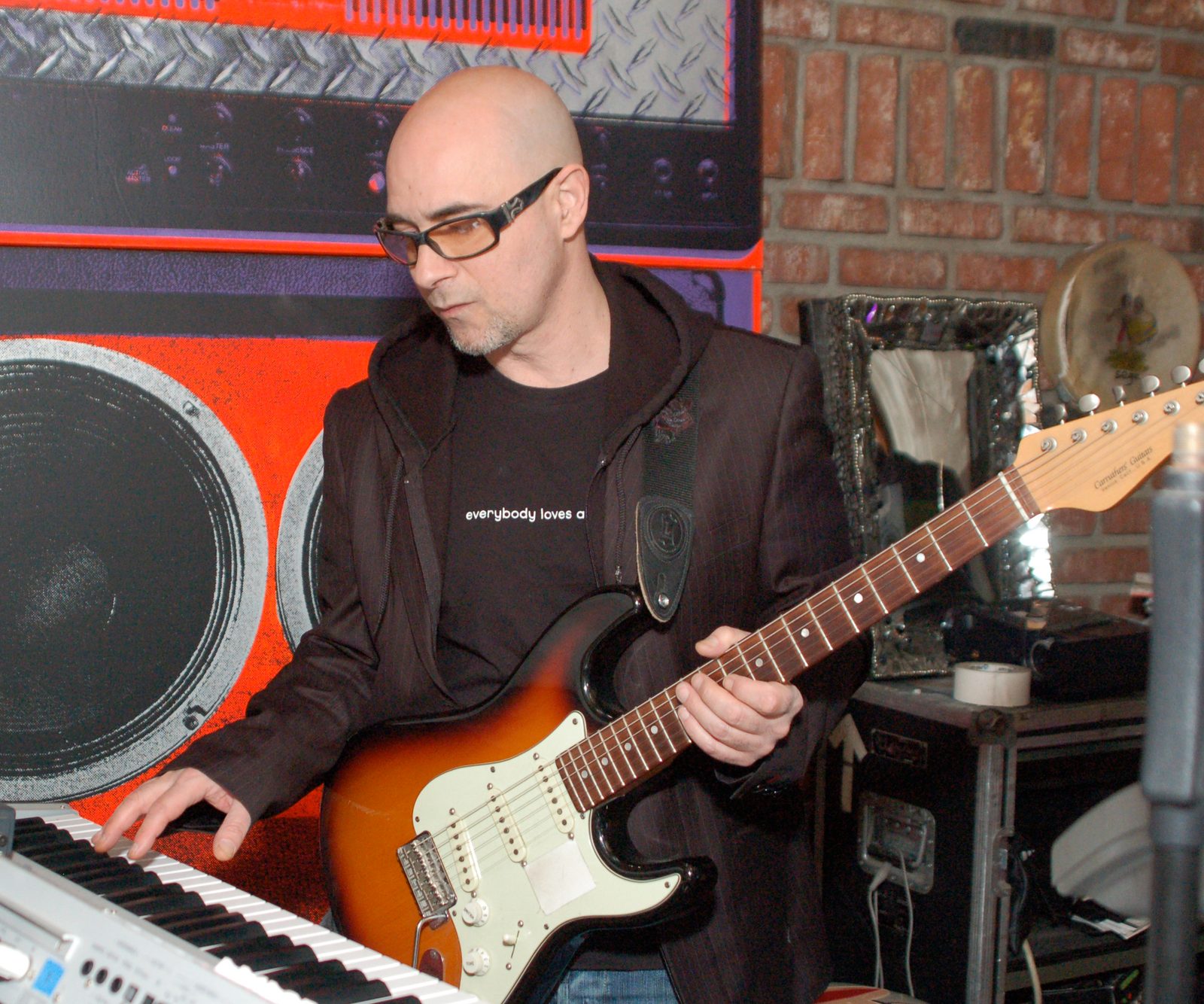 Warren Cuccurullo holding an electric guitar with one hand on a keyboard