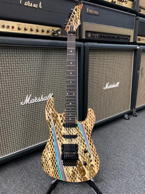A snakeskin-finish WRC electric guitar on a stand in front of Marshall amplifier cabinets